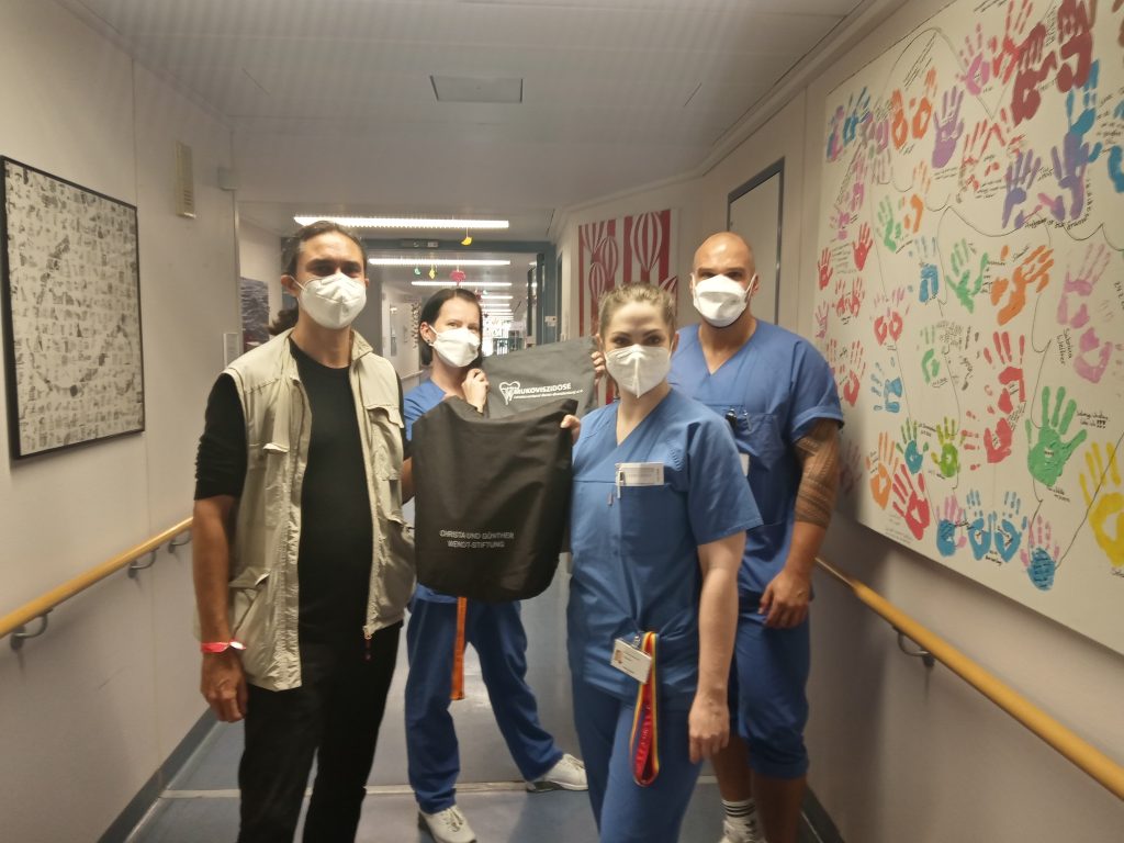 Gruppenfoto von einer Taschenübergabe in der Charité von zwei Menschen an zwei Bedienstete in blauer Dienstkleidung