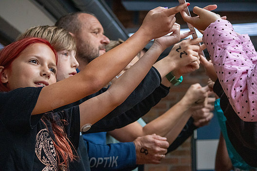 Gruppe von Menschen balancieren spielerisch einen Zollstock auf ihren Fingern