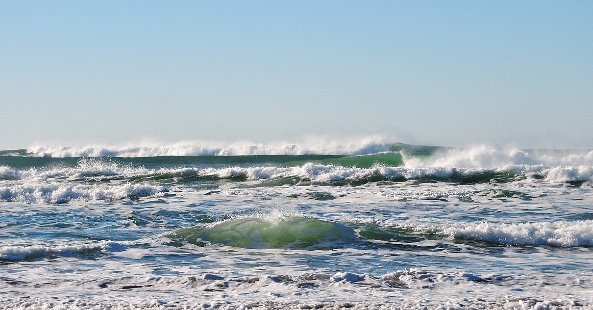 Wellen brechen am Strand unter klarem Himmel
