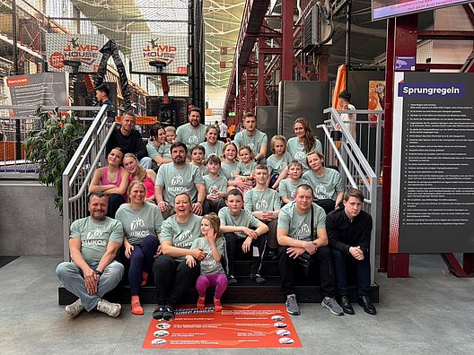Gruppe von Menschen in hellen T-Shirts sitzt und steht auf einer Treppe in einem Innenraum