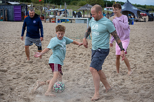 Kinder und Erwachsene spielen gemeinsam mit einem Fußball am Strand