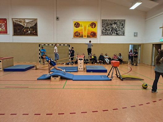 Turnhalle mit mehreren Kindern, die unter Aufsicht an verschiedenen Geräten turnen