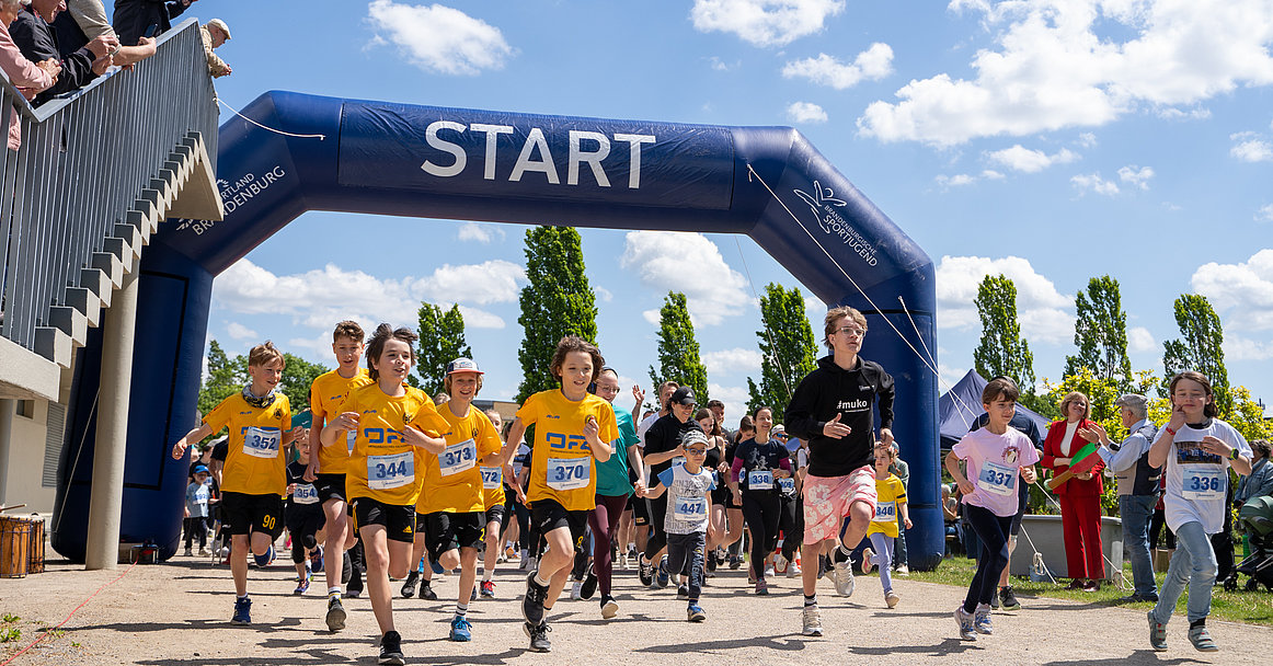 Kinder laufen durch den Startbogen beim Muko-Freundschaftslauf